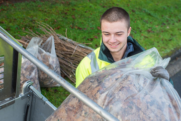 young worker loading bag of dead leaves into vehicle