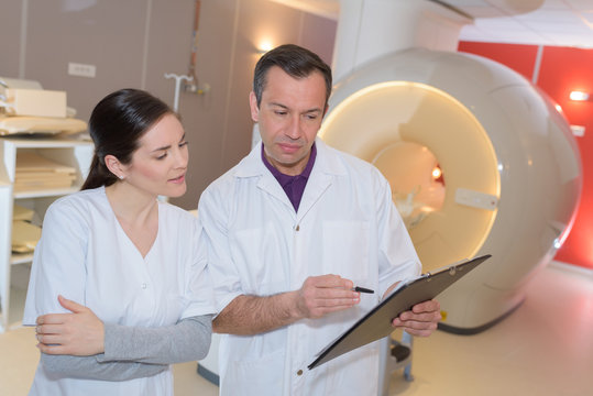 doctor standing arms crossed by patient lying on mri machine