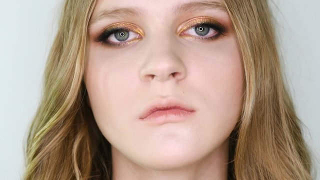 Close up portrait of beautiful young woman face with bright bronze make up looking at camera, then in front. Girl showing eye make-up