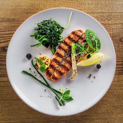 Salmon fish stake cooked on a grill with healthy salad on a plate. Healthy food made of fish and vegetables on a table. Top view.