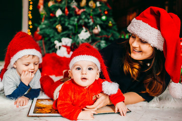Fototapeta na wymiar Mom and her sons in red hats lie before Christmas tree