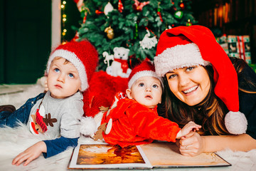 Mom and her sons in red hats lie before Christmas tree