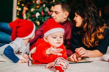 Mom, dad  and their sons in red hats lie before Christmas tree