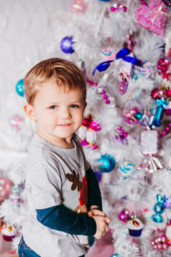 Little boy stands before a white Christmas tree with pink and blue toys