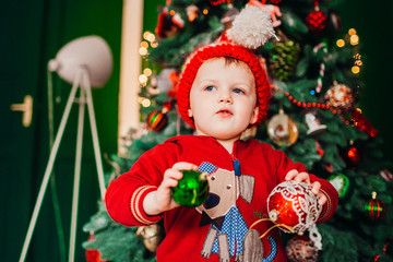 Little boy in red suit stands before a Christmas tree