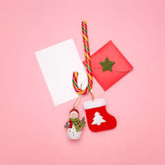 Christmas mockup. New Year postcard concept. Top view of a candy cane, a snowman, a Christmas sock, and an envelope on a pastel pink background. 