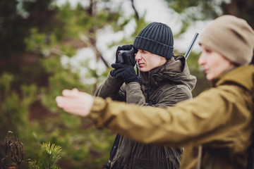 male and woman hunters ready to hunt, holding gun and walking in forest.