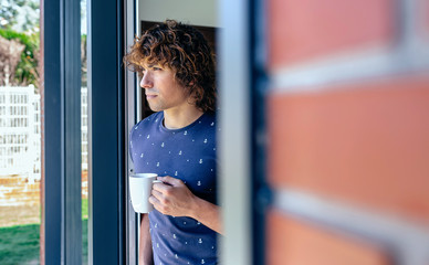 Man drinking coffee leaning against the window frame of his new home