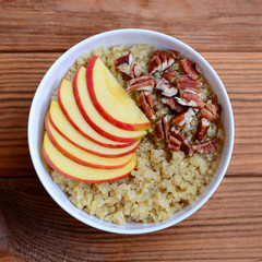 Fruit and nut Breakfast quinoa porridge. Quinoa porridge with fresh apples and pecans in a white bowl isolated on wooden background. Closeup. Top view