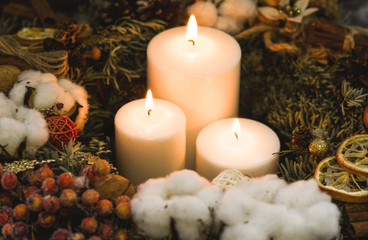 White burning christmas candles with pine twigs, pinecones and lemons