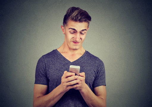 Upset man holding cellphone disgusted with message he received isolated on gray background.