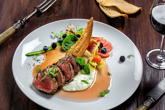 Medium rare meat steak medallions with sauce and salad on a plate. Delicious healthy food made of meat with vegetables and wine for lunch.