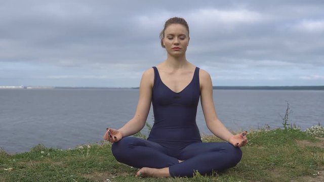 Female in classical yoga pose, energy concentration, cloudy sky and lake on background. Yogi training, outdoor meditation and healthy lifestyle