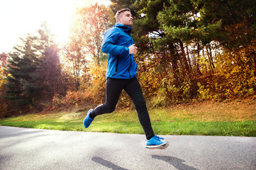 Young athlete running in park in colorful autumn nature.