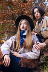 Fototapeta na wymiar Fashion portrait of two beautiful women in autumn landscape. Trendy indian coat and hat with scarf. Fashion autumn concept.Closeup
