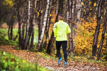 Young athlete with smartphone running in park in autumn.