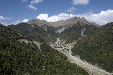 Azerbaijan, Greater Caucasus, near Gabala, Durca: Scenic panoramic view with village, gorge, rocky mountain chain, green trees, blue sky and white clouds. 