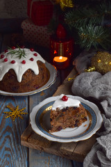 Traditional english Christmas steamed pudding with winter berries, dried fruits, nut in festive setting with Xmas tree and burning candle. Fruit cake