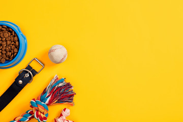 Toys -multi coloured rope, ball and dry food. Accessories for play on yellow background top view