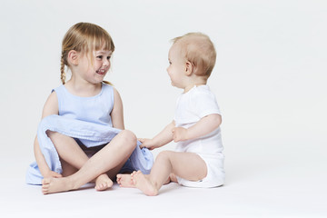 Brother and sister playing in white studio, smiling