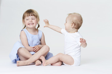 Baby boy and sister playing in white studio