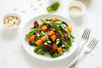 Fresh autumn salad with marinated pumpkin and beetroot, spinach leaves,olive oil, sesame and pumpkin seeds on white table cloth. Space for copy