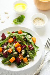 Fresh autumn salad with marinated pumpkin and beetroot, spinach leaves,olive oil, sesame and pumpkin seeds on white table cloth. Space for copy