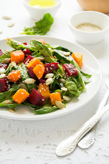 Fresh autumn salad with marinated pumpkin and beetroot, spinach leaves,olive oil, sesame and pumpkin seeds on white table cloth. Space for copy
