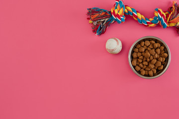 Toys -multi coloured rope, ball and dry food. Accessories for play on pink background top view