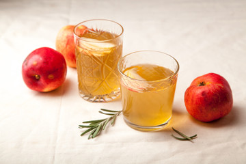 Two vintage glasses with apple cider on black background. Christmas beverages concept. Two red apples and rosemary sprig aside.  Warm backlight.