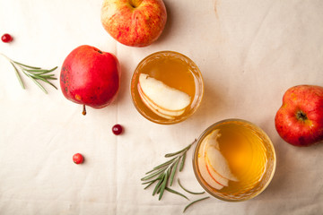 Two vintage glasses with apple cider on black background. Christmas beverages concept. Two red apples and rosemary sprig aside.  Warm backlight. Top view.