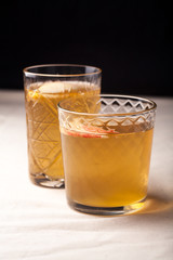 Two vintage glasses with apple cider on black background. Christmas beverages concept. Two red apples and rosemary sprig aside.  Warm backlight. Vertical composition.