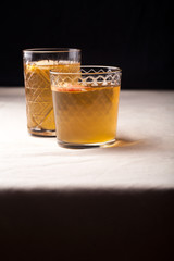 Two vintage glasses with apple cider on black background. Christmas beverages concept. Two red apples and rosemary sprig aside.  Warm backlight. Vertical composition.