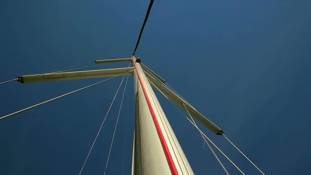 Sailing boats main mast with windex and supporting steel ropes. Shot from start of the mast looking upwards to blue sky.