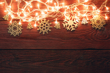Obraz premium Photo of New Year's wooden red background with burning garland from above, snowflakes