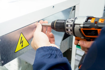 Carpenter working with an electric screwdriver on the metal device. CAUTION Danger sign. Toned with sunlight - 181626105