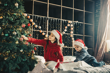  Couple kids Little girl and boy  in santa klaus hat decorating xmas tree. Merry Christmss and...