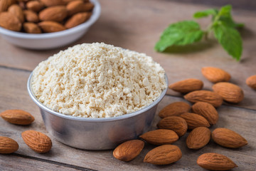 Almond flour in bowl and almonds on wooden table