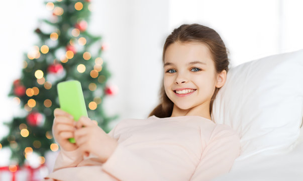 happy girl in bed with smartphone at christmas