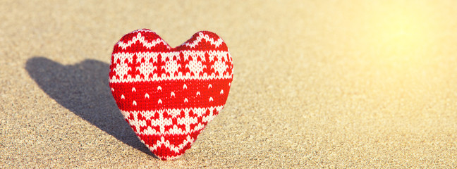 red knitted heart on sea sand