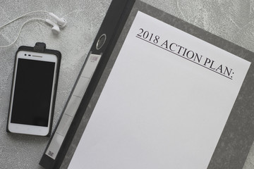 2018 action plan paper on a gray office folder, a mobile phone with headphones on a ligth concrete background, top view