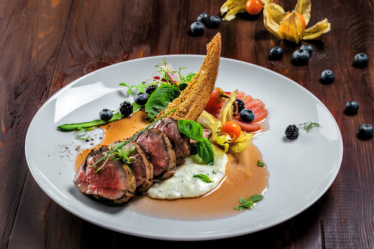 Plate with medium rare meat steak, sauce and salad on a wooden table. Healthy gourmet food made of meat fillet and fresh vegetables.