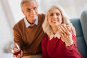 Dreams come true. Selective focus on a hand of a retired lady showing her ring with a diamond while sitting next to her fiance and getting excited over the engagement.