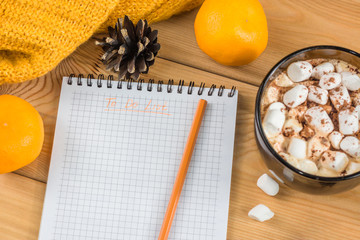 Cup of hot cocoa or chocolate with marshmallow, holiday decorations and notebook with to do list on wooden table, christmas planning concept.