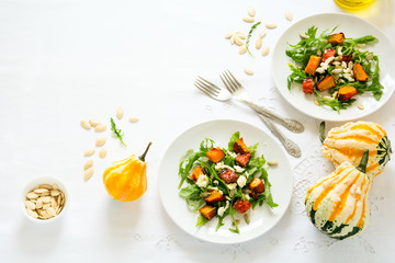 Fresh autumn salad with baked pumpkin, arugula, cheese and seeds on white table cloth. Space for copy