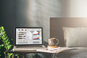 Fototapeta premium Workplace in bad room without people, close-up of laptop with graphs, charts, diagrams on screen on table.Nearby is newspaper, cup of coffee.On background bad, pillow. Mock up.Nobody.Online marketing.