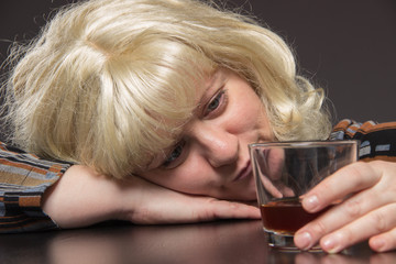 Lonely middle-aged woman drinks some brandy alcohol and head on the table