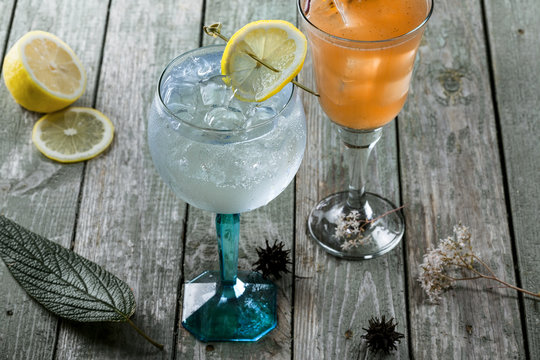 Alcoholic gin and tonic cocktail with drink made of rum, soda, ice and basil leaf in a long glass on a wooden table.