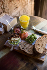 Soft focus shot of tasty delicious meal, breakfast with wholewheat bread, avocado, salmon and chia seeds with fruits, served on hipster artisan wooden board and orange juice at cool cafe