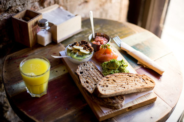 Soft focus shot fancy breakfast served on artisan wooden cutting board at downtown cafe or restaurant, with wholewheat bread, avocado spread and fresh pressed orange juice, tasty treat
